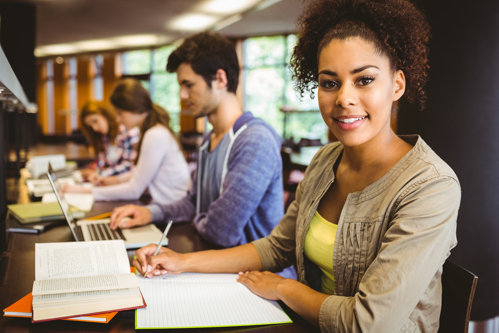 Student looking at camera while studying with classmates in library-3